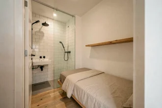 Petite chambre de moins de 9m² avec salle d'eau intégrée séparée par une cloison en verre
